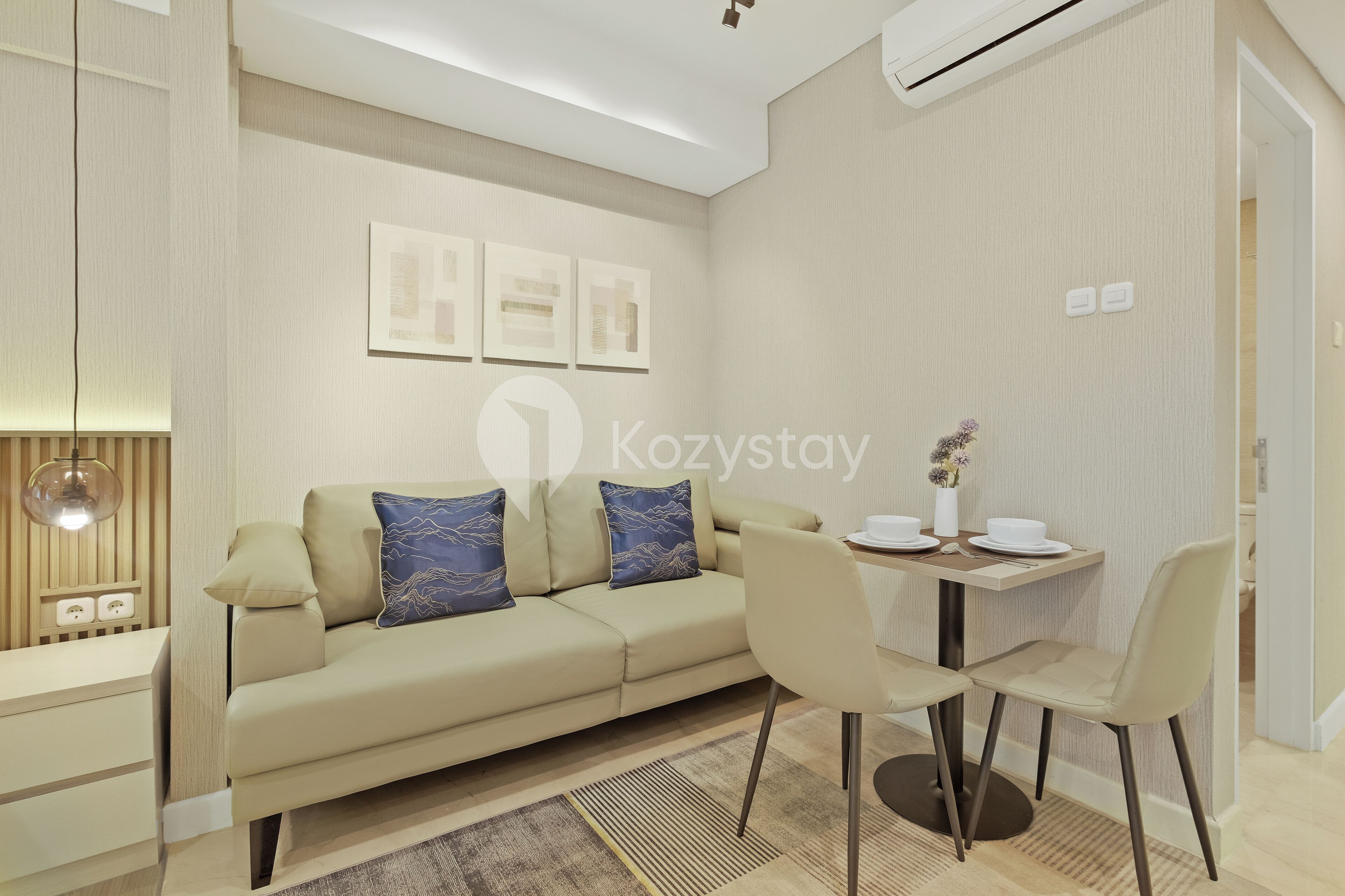 A modern living room with a sofa, two chairs, a small table with a vase, and framed pictures on the wall.