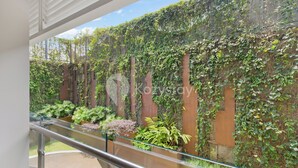 Une vue depuis un balcon doté d’une rambarde en métal, donnant sur un jardin avec différentes plantes et un mur recouvert de lierre.