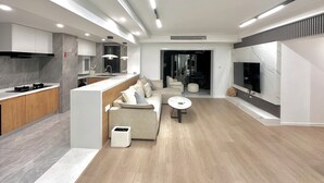 A modern kitchen with a built-in island, a seating area with a sofa and coffee table, and a TV mounted on the wall. - ZHome-Sun Garden-Amazing view (Shanghai)