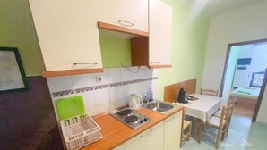 A compact kitchen with a stove, sink, and a dining area with a table and chairs. - Apartment Dea 1 (Jadranovo)
