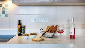 Una encimera de cocina con tabla de cortar, queso, aceitunas, pan, una botella de vino y una copa de vino.