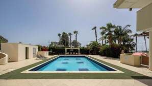 Piscina con agua azul cristalina, rodeada de palmeras y una pérgola.