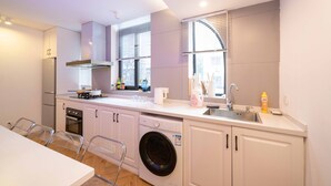 A compact kitchen with a dishwasher, oven, and washing machine. It includes a sink, countertop, and a window with blinds. - ZHome-Three floors 4 bedrooms (Shanghai)