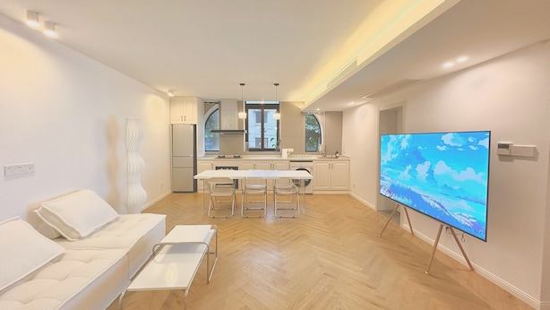 A modern living room with a sofa, a TV on a stand, and a kitchen in the background. - ZHome-Three floors 4 bedrooms (Shanghai)