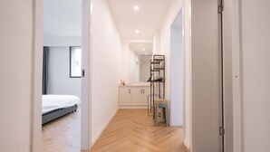 A hallway with a wooden floor leading to a bedroom with a bed and a bathroom with a sink and shelves. - ZHome-Three floors 4 bedrooms (Shanghai)