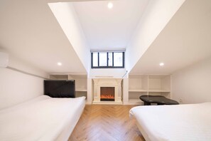 Une chambre avec une cheminée, deux lits, une télévision et une fenêtre.