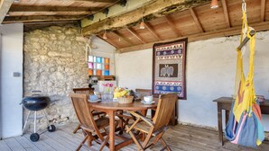 A wooden dining table with chairs, a hanging hammock, and a stone wall. - House for 4 with garden - 500m from the beach (Barbâtre)
