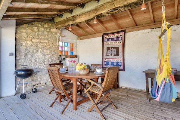 Una mesa de madera con sillas, una hamaca colgante y una pared de piedra.