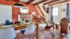 A dining area with a wooden table, white chairs, a patterned rug, and a staircase leading to another level. - House for 4 with garden - 500m from the beach (Barbâtre)