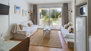A living room with a sofa, a coffee table, and a TV. There is a sliding glass door leading to an outdoor area with chairs and a table. - Apartment -450m from the beach- swimming pools (La Baule-Escoublac)