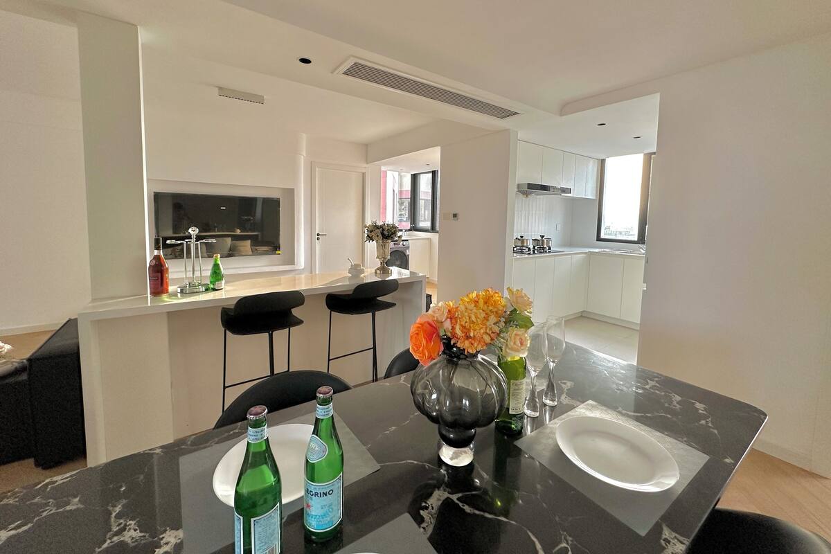 A modern kitchen with white cabinets, a black countertop, and a dining area with a black table and chairs.