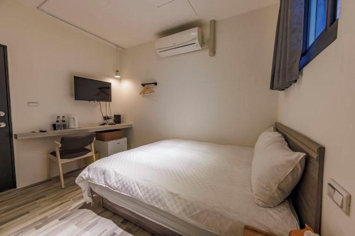 A bedroom with a bed, a desk, a chair, a TV, and an air conditioning unit.