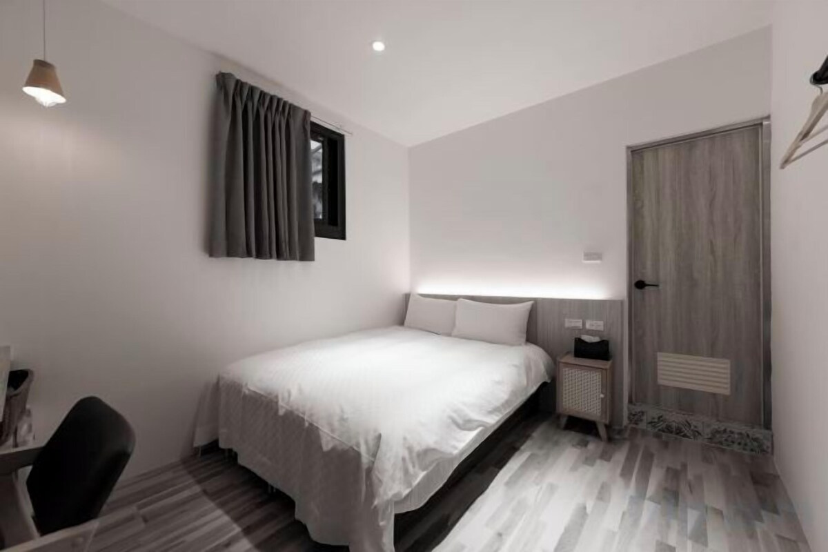 Ein Schlafzimmer mit Bett, Nachttisch, Lampe und einer Tür.