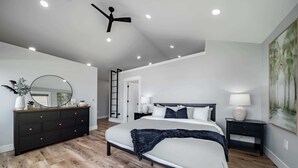 Un dormitorio moderno con una cama grande, un aparador, un espejo y un ventilador de techo.