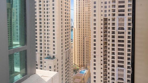 A high-rise building with multiple floors, large windows, and a pool area visible in the lower part. - Ethereal 1 BR in JBR (Dubai)