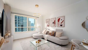 A modern living room with a large window, a sofa, a glass coffee table, and abstract wall art. - Ethereal 1 BR in JBR (Dubai)
