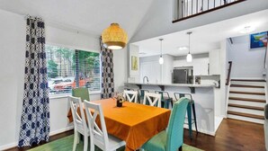A dining area with a table set for four, white chairs, a patterned curtain, and a hanging light fixture.