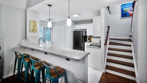 A modern kitchen with a central island, bar stools, and a staircase leading to another level.