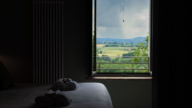 A bedroom with a large window overlooking a green landscape. - Retrocantina (Montefalco)