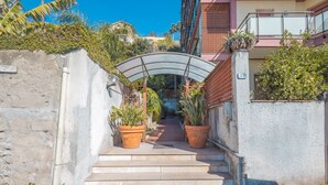 Un chemin menant à l’entrée d’un bâtiment, avec des marches, des plantes en pot et un auvent en métal.