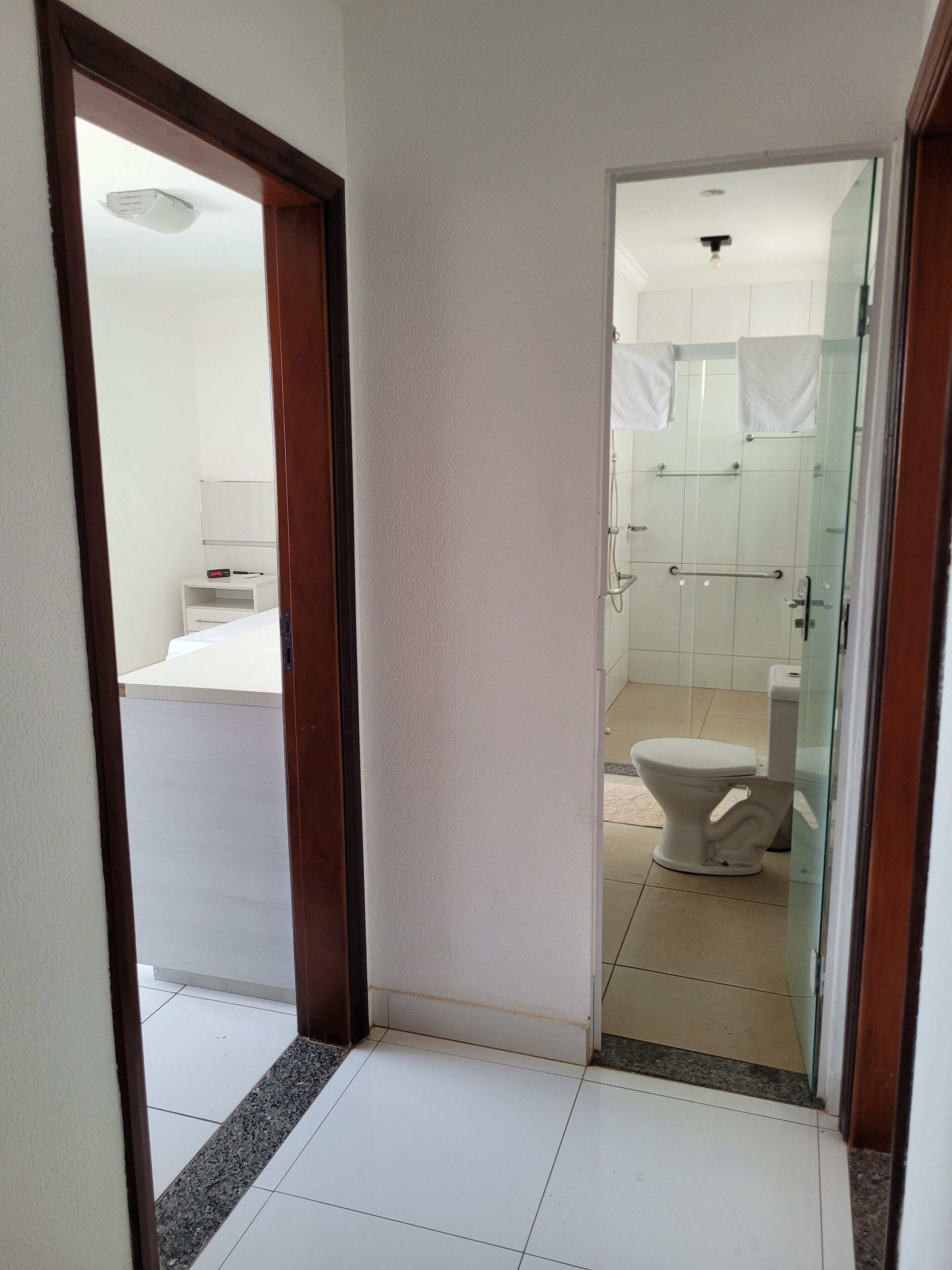 Pasillo que conduce a un baño con inodoro, zona de ducha y un pequeño armario blanco con espejo.