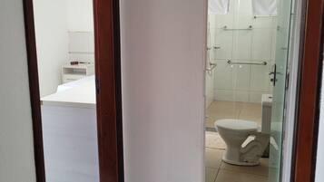 Pasillo que conduce a un baño con inodoro, zona de ducha y un pequeño armario blanco con espejo.