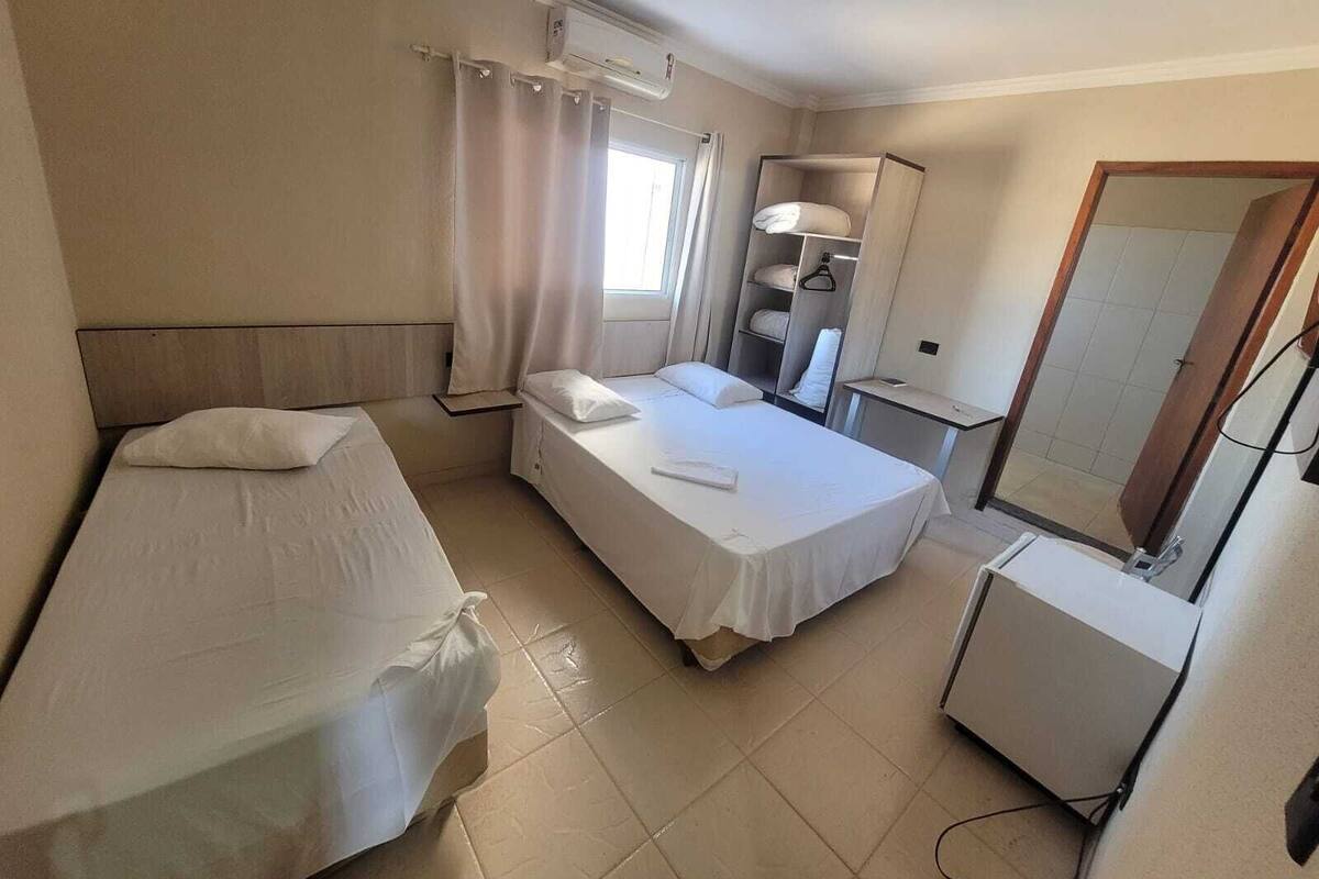 Una habitación de hotel con dos camas individuales, un armario, un escritorio y un espejo.