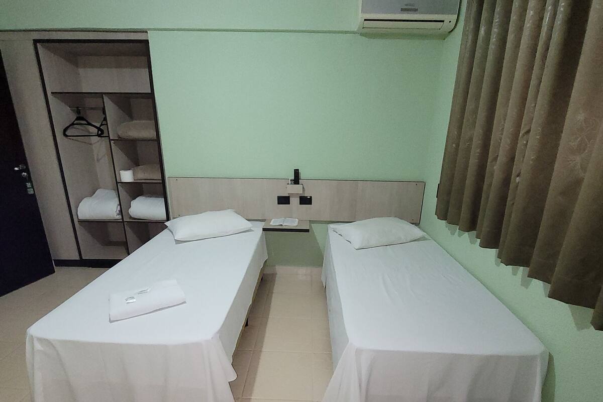 Una habitación de hotel con dos camas individuales, un armario, un calentador y una cortina.