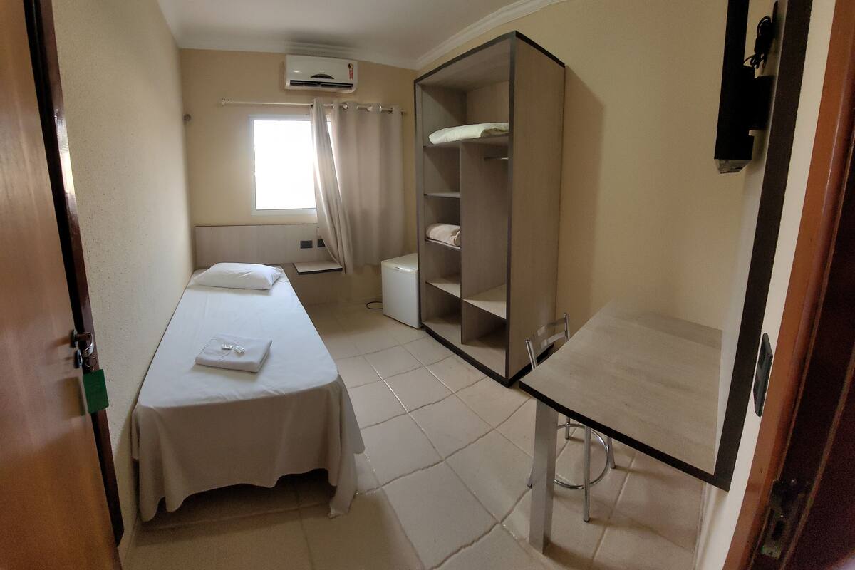 Una habitación de hotel con cama, un escritorio pequeño, un armario y un equipo de aire acondicionado.