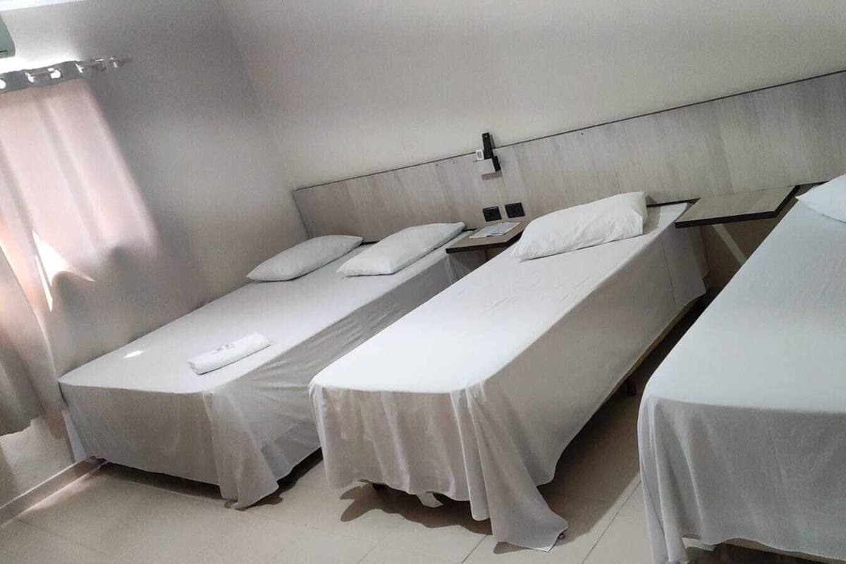 Una habitación con tres camas individuales, cada una con colchón y almohada blancos, y un cabecero.