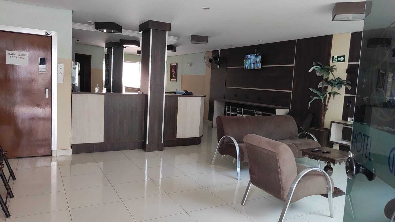 A hotel lobby with a reception desk, seating area, and a large screen.