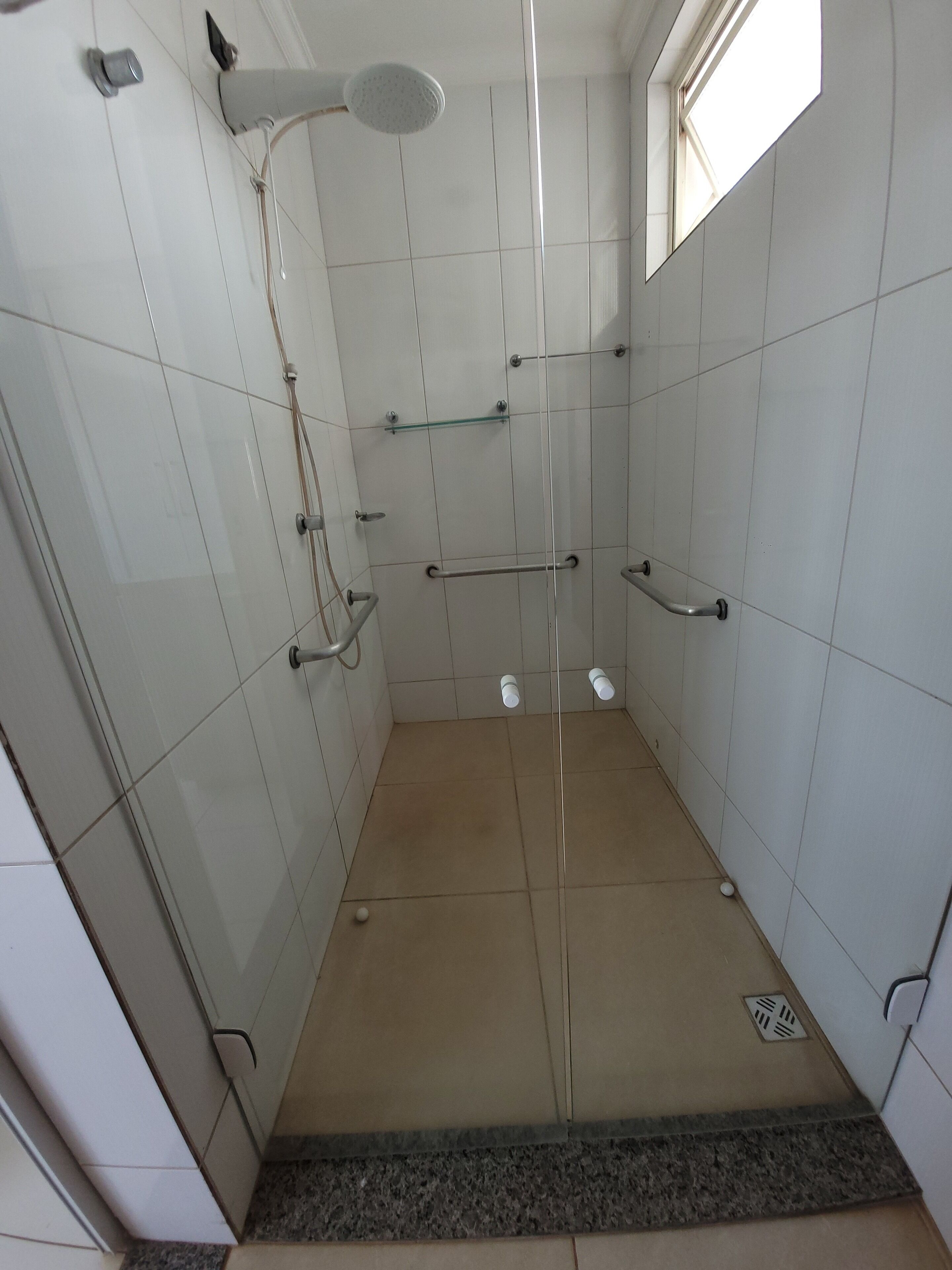 Une petite cabine de douche carrelée, dotée d’une porte en verre, d’un pommeau de douche et d’une barre d’appui.