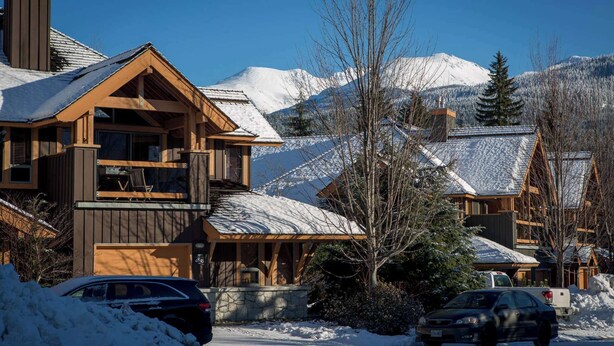 Eine Holzhütte mit Balkon, umgeben von schneebedeckten Bergen und Bäumen.