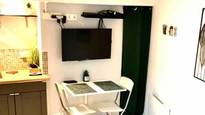 Une cuisine compacte avec un coin repas, un téléviseur à écran plat fixé au mur et une petite plante en pot.