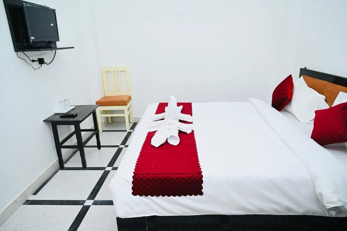 A hotel room with a bed, a small table, a chair, and a TV mounted on the wall.