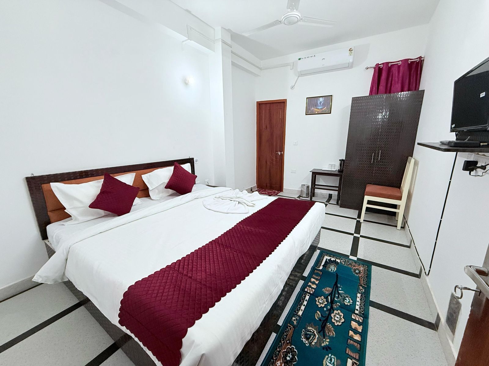 Una habitación de hotel con cama, escritorio, silla, televisor y armario.