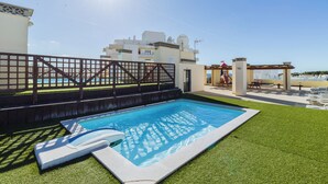 Una piscina con sombrilla, rodeada por una valla, y una vista de un edificio al fondo.