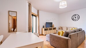 Un salón moderno con una mesa blanca, un sofá gris y un televisor sobre un mueble de madera.