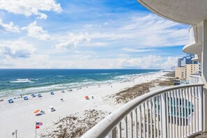 A beach with umbrellas and flags, a view of the ocean, and buildings in the background.