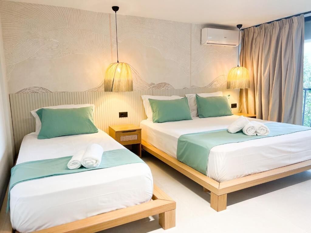 A hotel room with two beds, each with a headboard, bedside lamps, and a window with curtains.