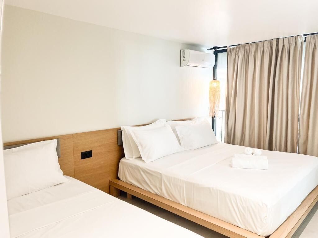 Ein Hotelzimmer mit zwei Einzelbetten, einem Nachttisch, einer Wand-Klimaanlage und einem Fenster mit Vorhängen.