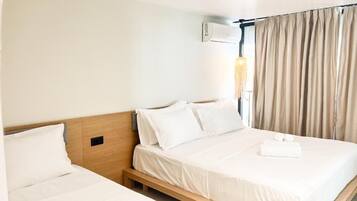 Ein Hotelzimmer mit zwei Einzelbetten, einem Nachttisch, einer Wand-Klimaanlage und einem Fenster mit Vorhängen.
