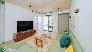 A living room with a flat-screen TV, wooden coffee table, green sofa, and a ceiling fan. - Fumba Town Private Residences (Kombeni)
