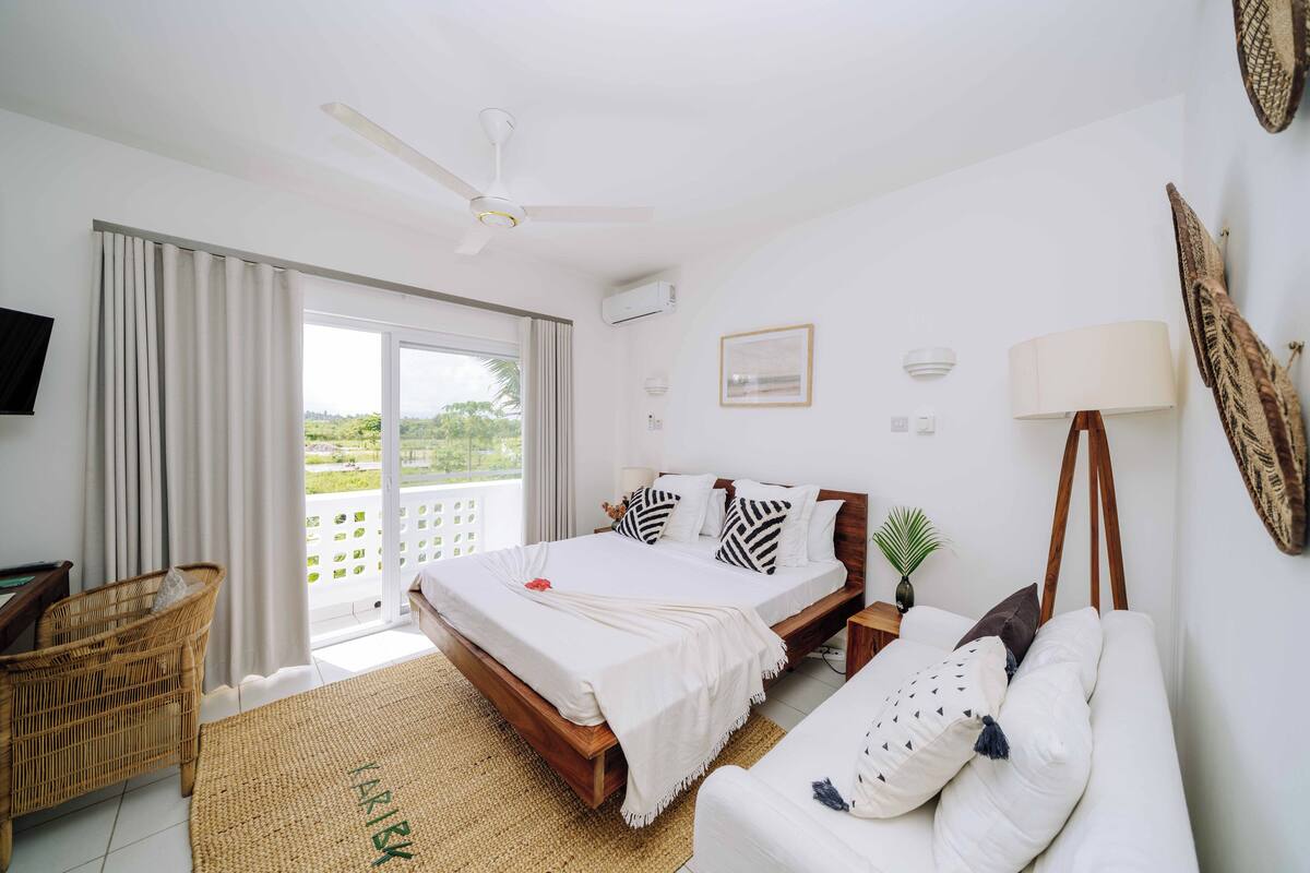 Une chambre à coucher comprenant un lit, un canapé, une chaise, un ventilateur de plafond et une vue sur l’extérieur.