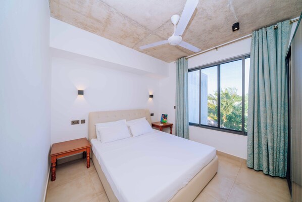 Ein Schlafzimmer mit einem Bett, einem Nachttisch, einem Deckenventilator und einem Fenster mit Vorhängen.