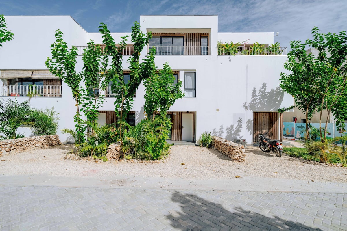 Un bâtiment moderne doté d’un toit plat, de nombreux balcons et d’un espace d’entrée pavé.