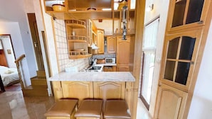 A compact kitchen with wooden cabinets, a built-in stove, and a small bar area with stools. - Apartman Talia 1 (Dramalj)