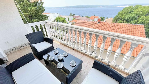 A balcony with wicker furniture, a table set for tea, and a view of the sea and buildings. - Apartman Talia 1 (Dramalj)