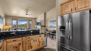 A modern kitchen with wooden cabinets, a stainless steel refrigerator, and a dining area with a view. - New! Old Mill Lookout–Mountain Views, Fireplace, Dog Friendly (Bend)