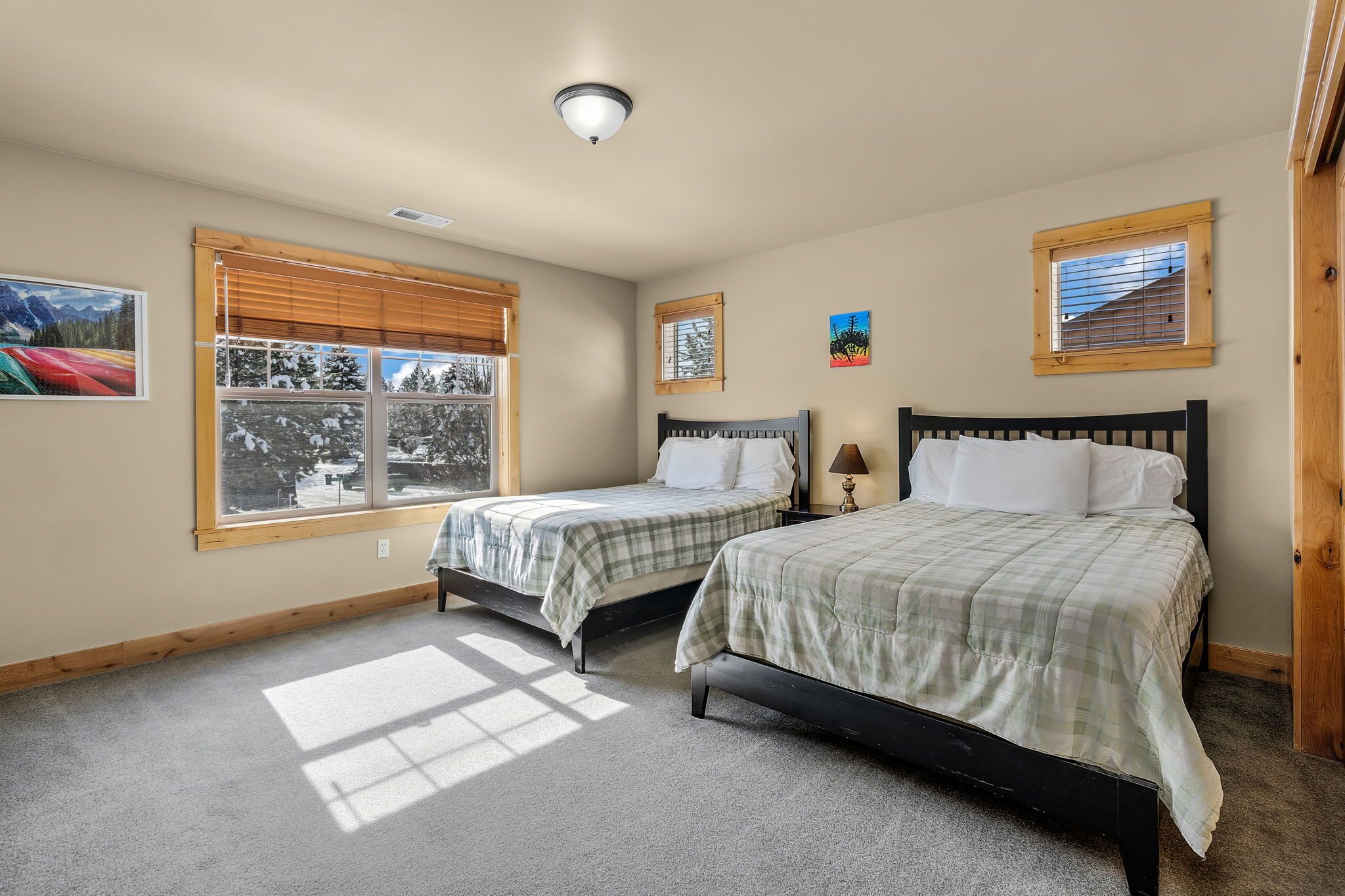 A bedroom with two beds, a window with blinds, a ceiling light, and a small picture on the wall.